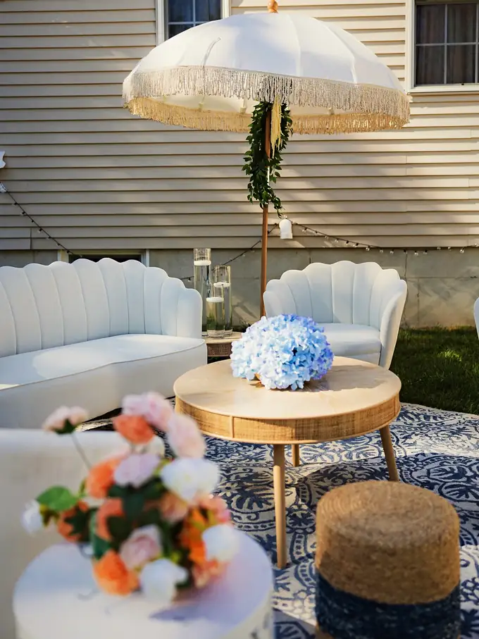 Backyard lounge with white scalloped sofas, a fringed umbrella, blue hydrangeas and coral roses for a garden celebration